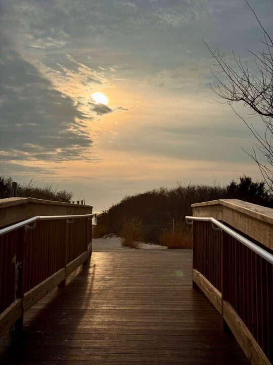 Late afternoon sun peeking through grayish blue clouds on a January day, walking onto the beach through a wooded dune trail.