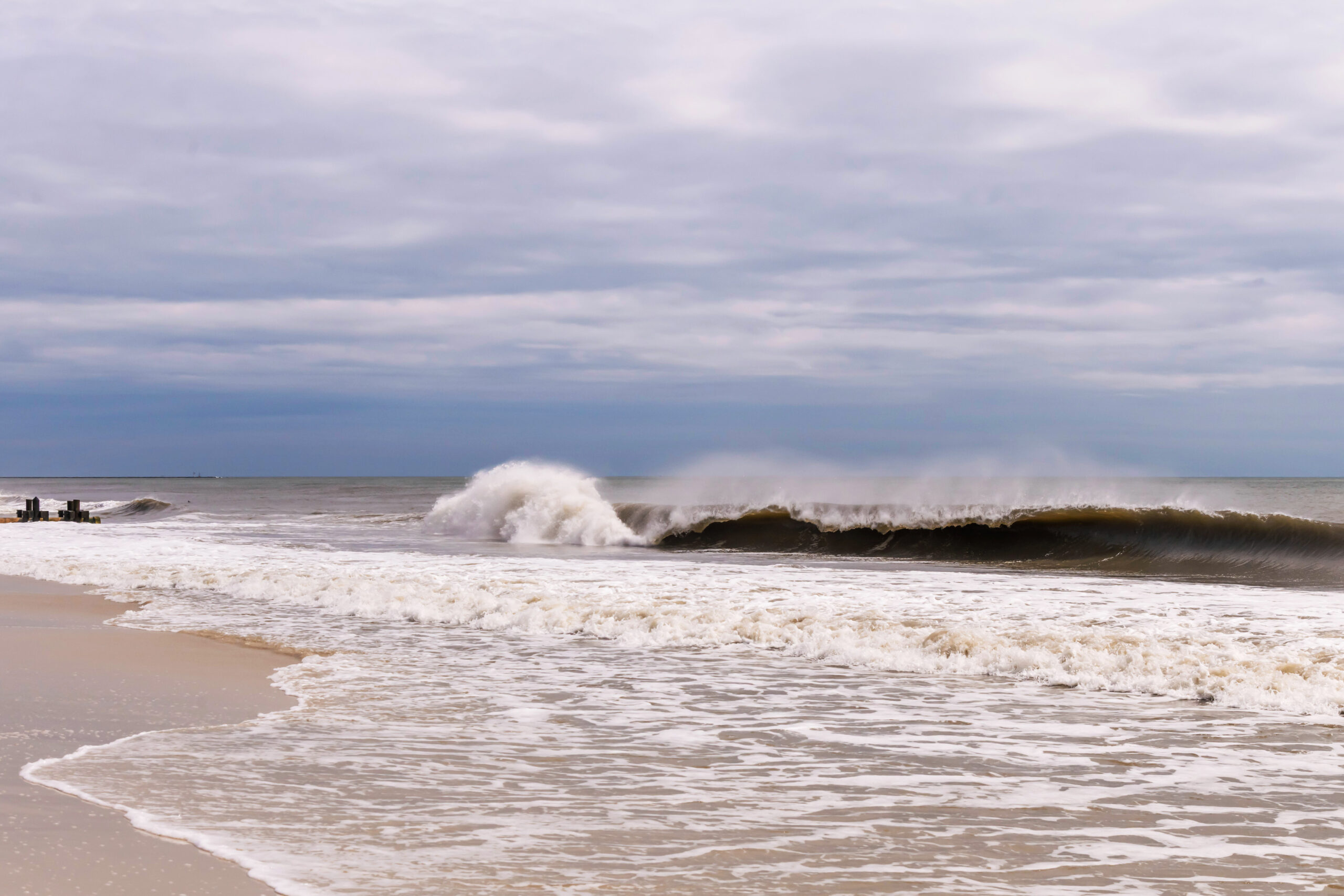A big wave crashing in the ocean at the beach with a cloudy sky.