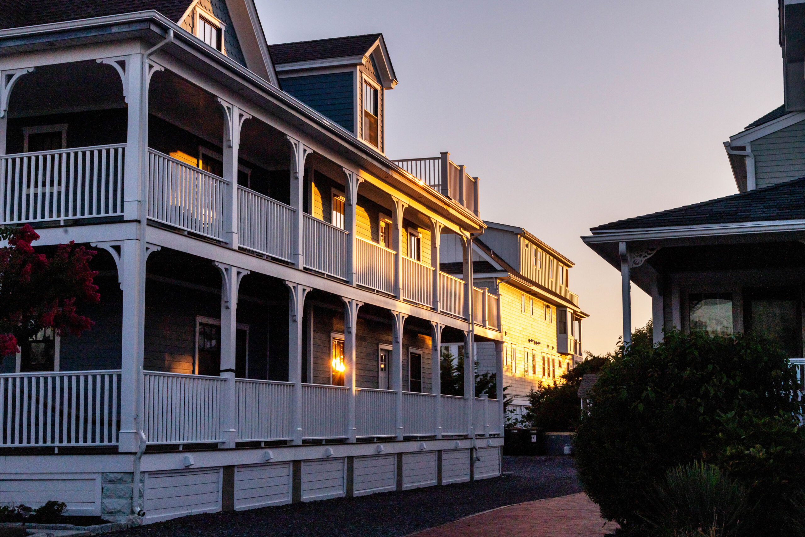A wide view of first and second floor porches on a Victorian home at sunset. The porches are lit up by sunlight.