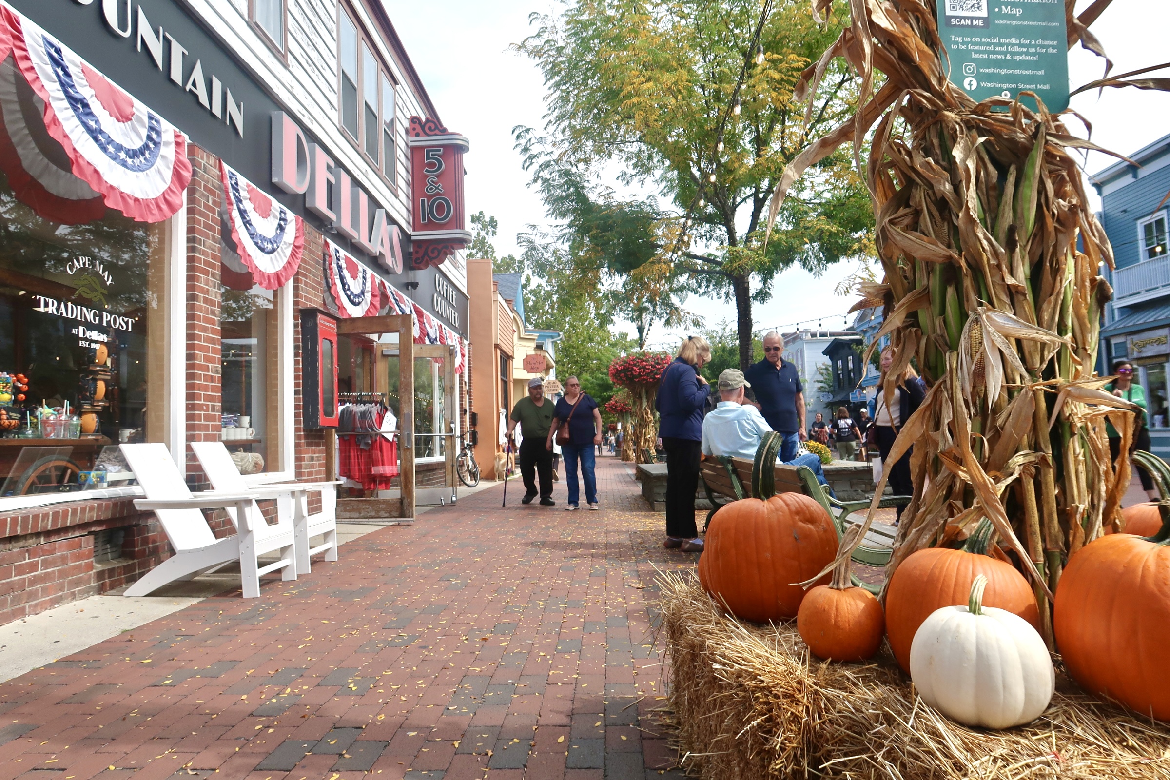 Fall leaves on the mall with stalks, pumpkins, and people out front of Dellas