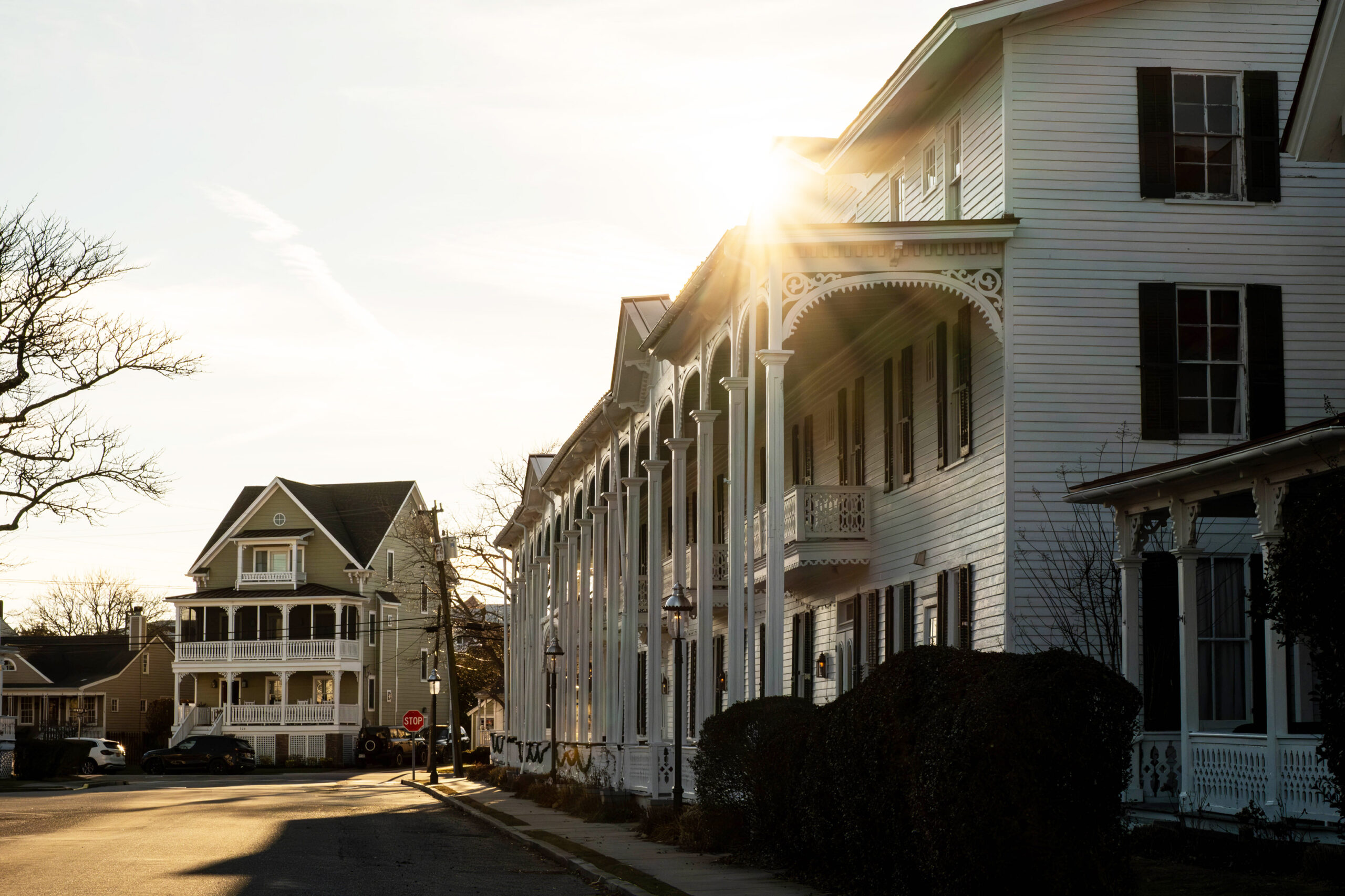 A wide view of the sun shining behind the Chalfont hotel. A Victorian home is at the end of the street.