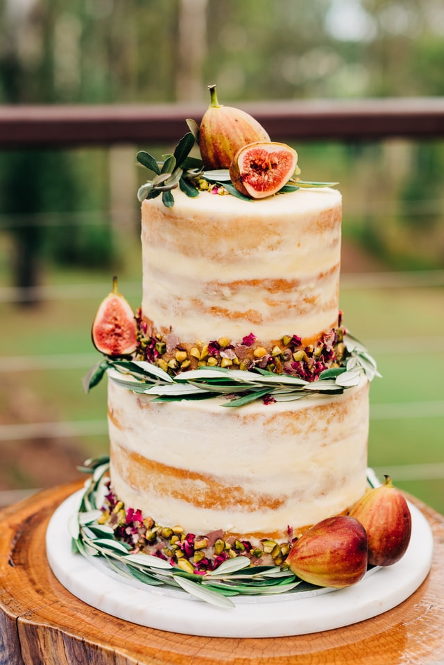 Two tier rustic wedding cake decorated with fresh figs, berries, and greens